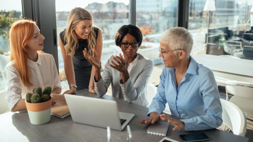 Four business women gather around a desk to share ideas